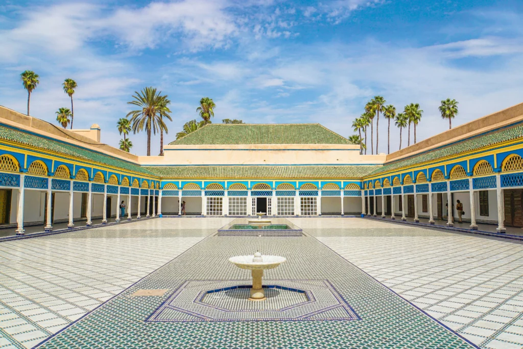 Wide view of the sunlit Grand Court of Bahia Palace with blue and yellow accents.