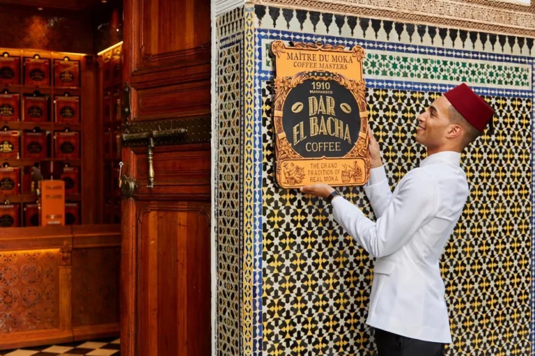 A server in white uniform hangs a vintage coffee sign on a zellige wall.