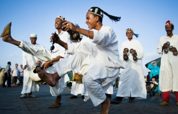 Gnawa musicians in traditional red dress play instruments in a public plaza.