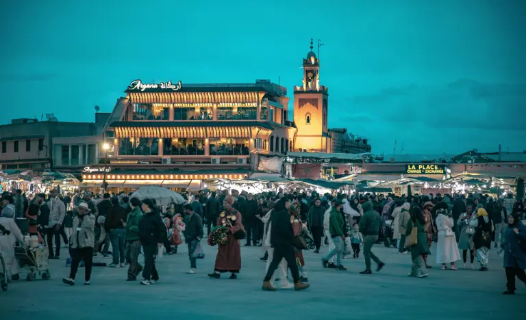 Crowded Jemaa el-Fna square in Marrakech at dusk with glowing buildings.