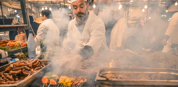 A chef prepares traditional food at a busy night market stall with rising steam.