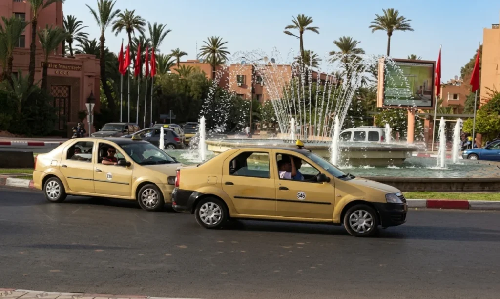 A row of yellow taxis is parked on a wet street next to an old stone wall.