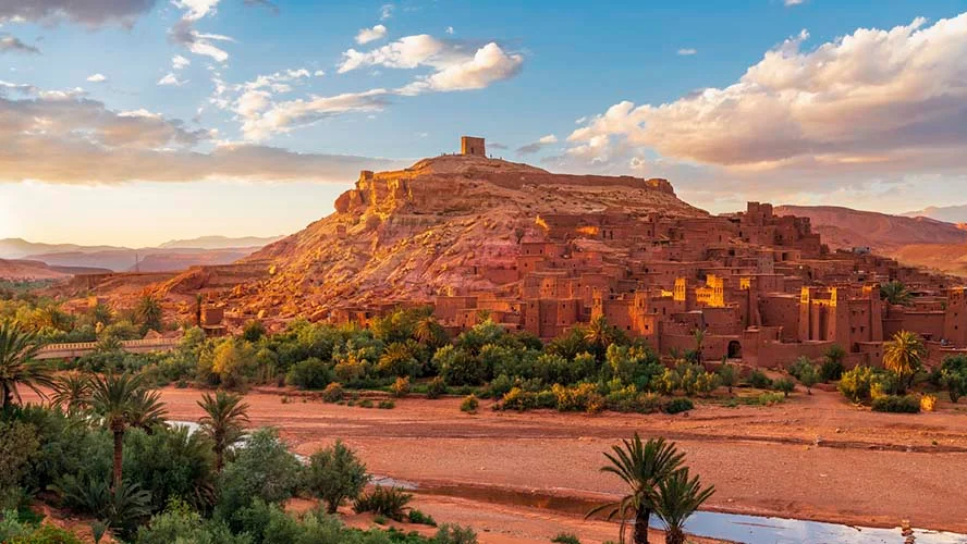 An ancient clay fortress city rising up a desert hill under a bright sky.