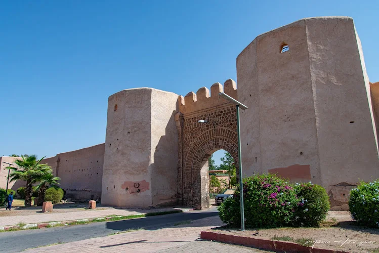 A grand stone archway set between thick, towering clay walls under a blue sky.