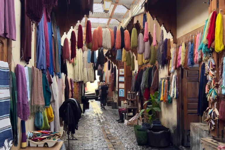 Skeins of vibrant, colorful dyed wool hanging above a narrow cobblestone alley.
