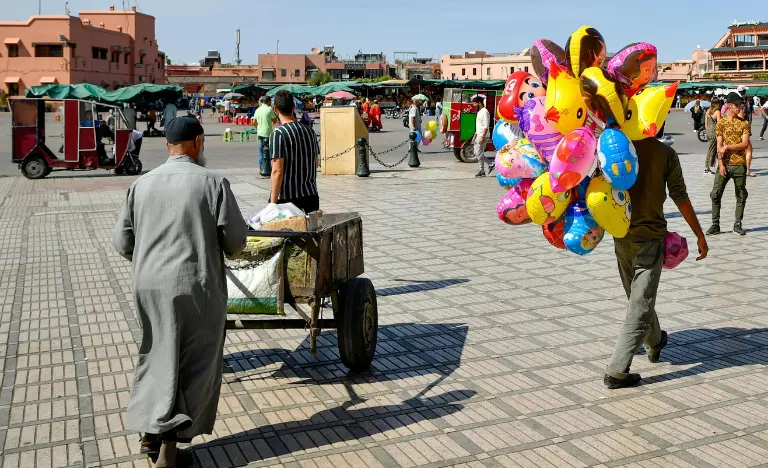 A man carrying a massive bunch of colorful balloons across an open square.