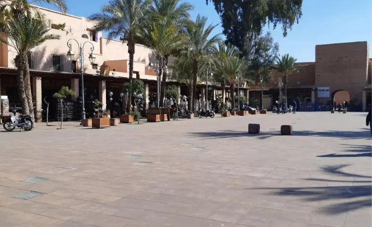 An open public square with palm trees and a large stone archway in the sun.