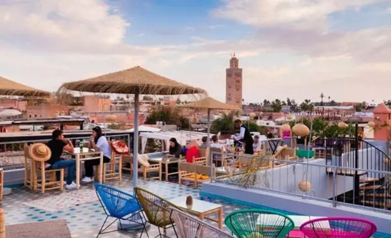 People dining on a lively rooftop terrace with a view of a distant minaret.