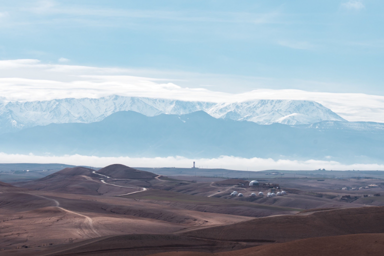 Paysage lunaire et aride du désert d'Agafay avec l'Atlas enneigé en perspective.