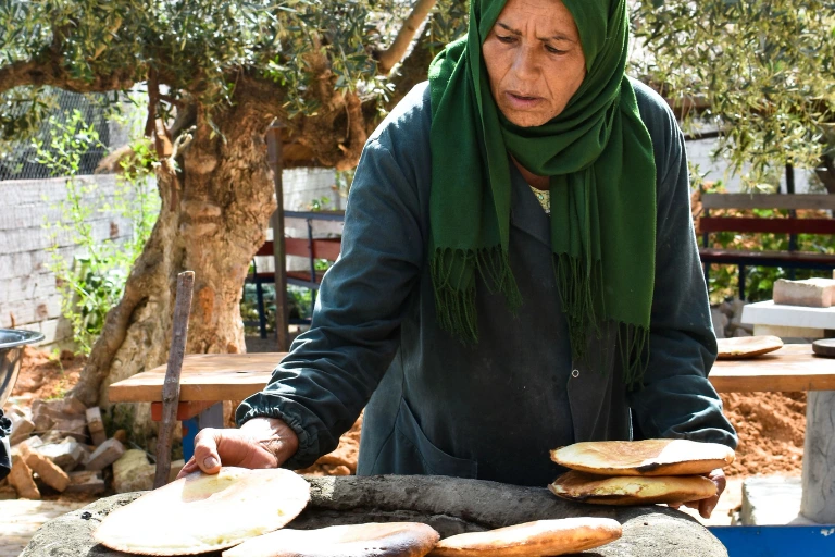 A woman baking fresh traditional khobz bread inside a rustic outdoor clay oven.