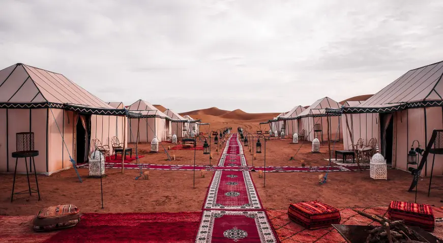 Luxury desert campsite with traditional tents and red carpets on the sand.