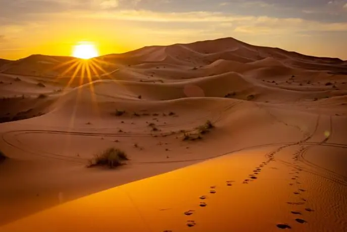 Golden sunset over desert sand dunes with footprints leading into the horizon