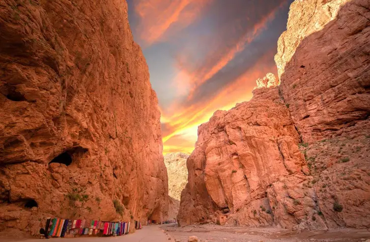 Tall red canyon rock walls under a bright sunset sky in a desert gorge valley