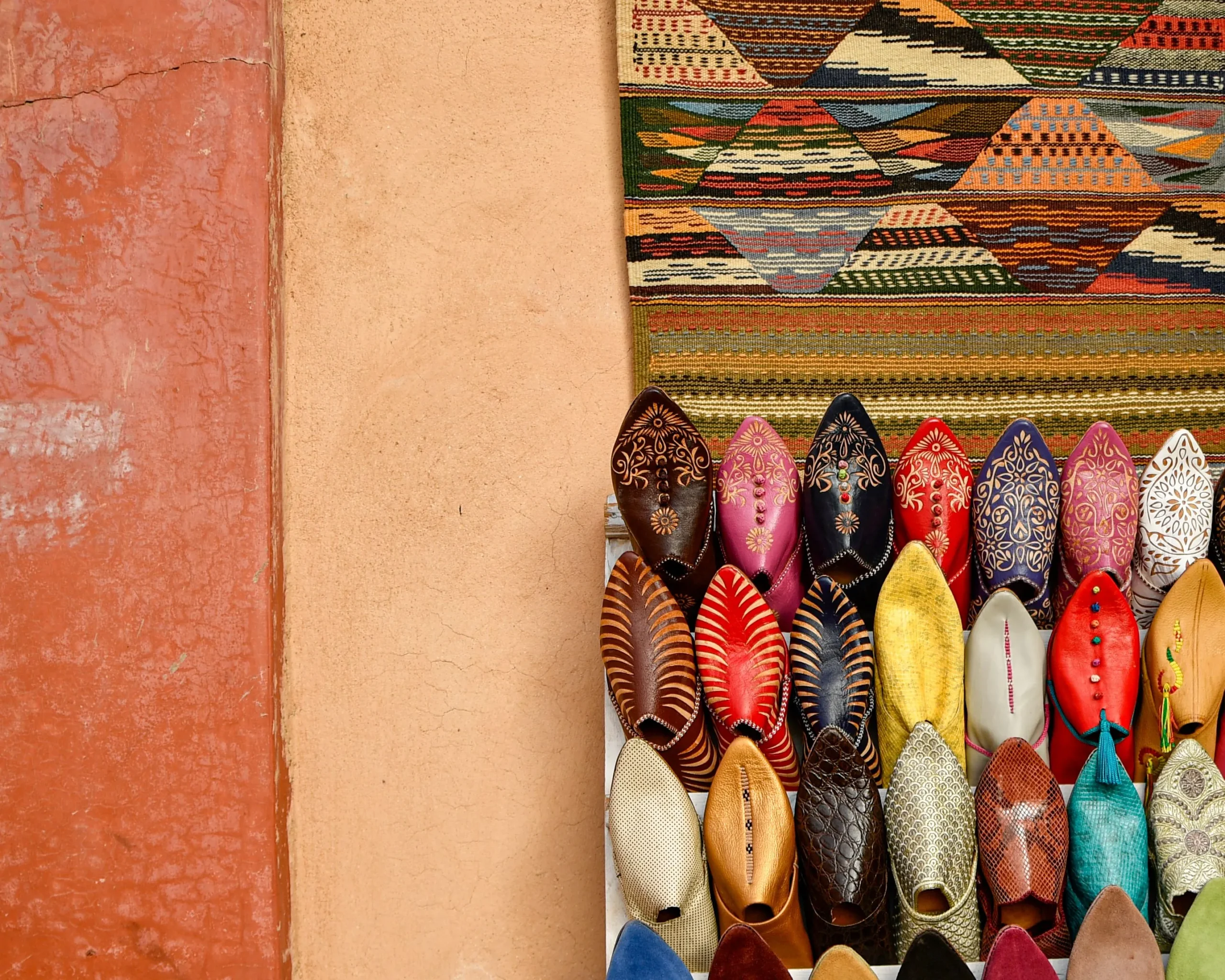 Colorful handmade leather babouches below a woven Berber rug on a red wall in the Marrakech souk