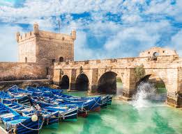 Tourists walk past blue fishing boats in the historic port.